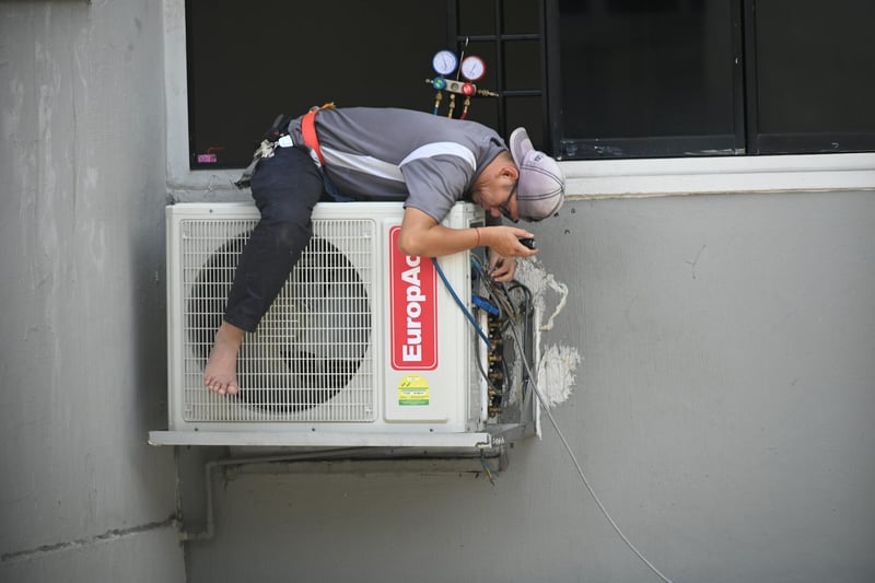 A technician leaning over an outdoor air conditioning unit to service it